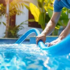 Commercial Swimming Pool Service: Daily, Weekly, and Monthly Tasks Explained Commercial Swimming Pool Service technician cleaning a pool using a vacuum hose under bright outdoor sunlight